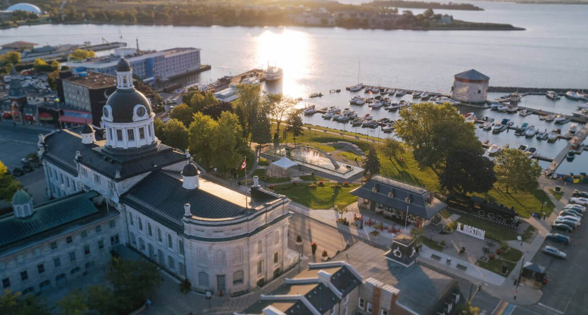 Aerial view of Kingston, Ontario, waterfront at sunset, showing City Hall, Confederation Park, and the marina.